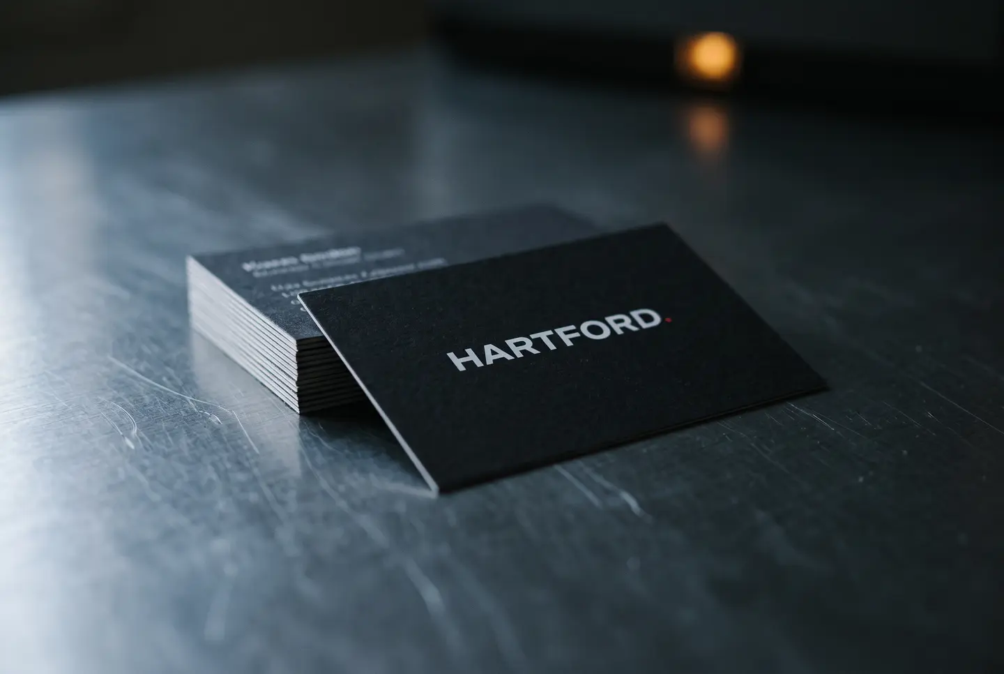 A stack of matte black business cards on brushed steel, the top card carrying the Hartford wordmark in white.
